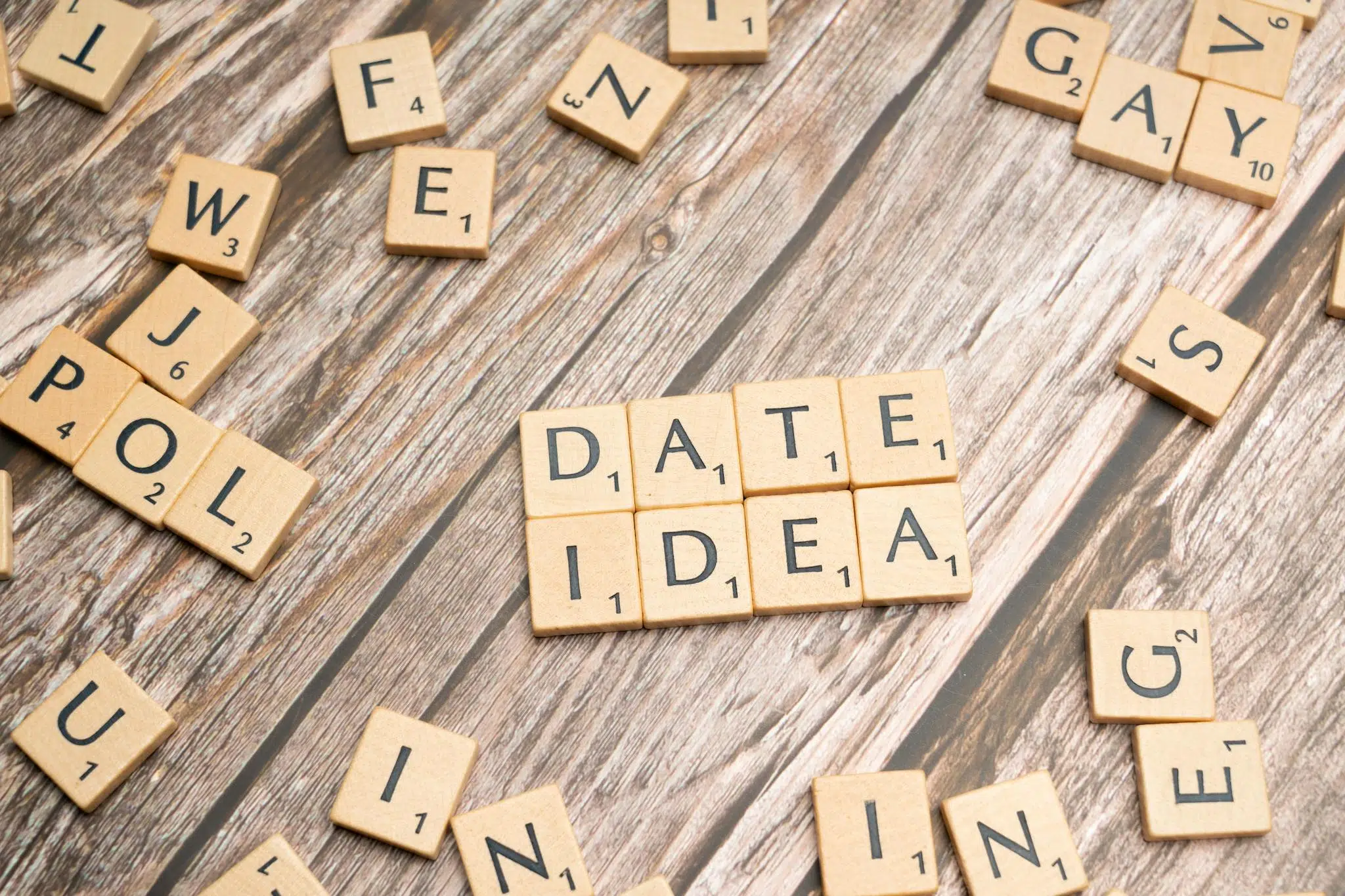 Our Mission 2 Letter tiles spelling 'Date Idea' on a wooden surface, suggesting creative meeting plans.